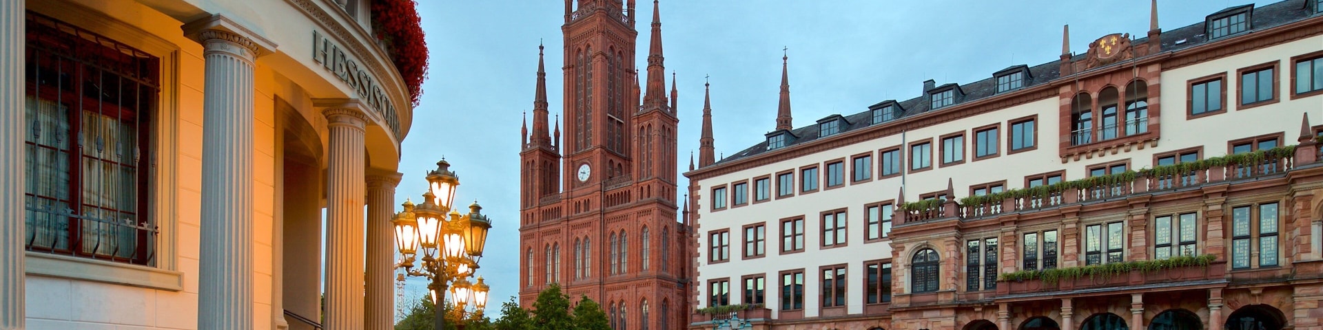 A cobblestone square with historic buildings, a church tower, and a chessboard sculpture.