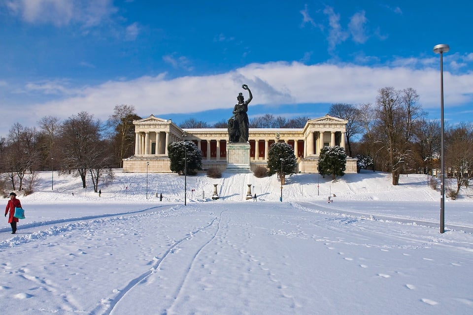 Un parque cubierto de nieve con un edificio clásico y una estatua en el centro.