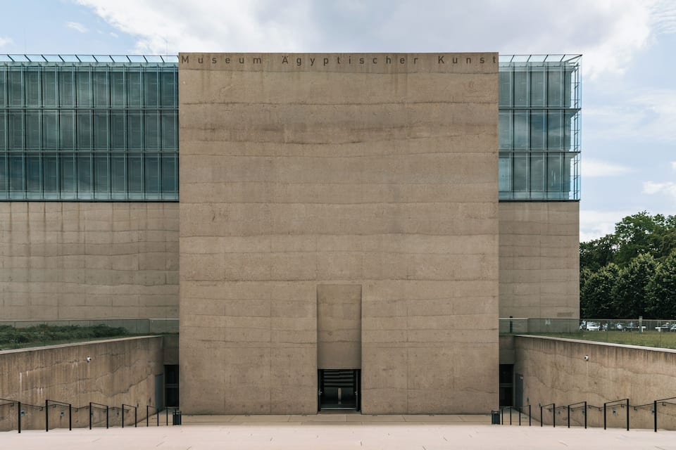 Um edifício moderno com uma entrada central ampla, janelas de vidro e uma placa com a inscrição 'Museum Agyptischer Kunst'.
