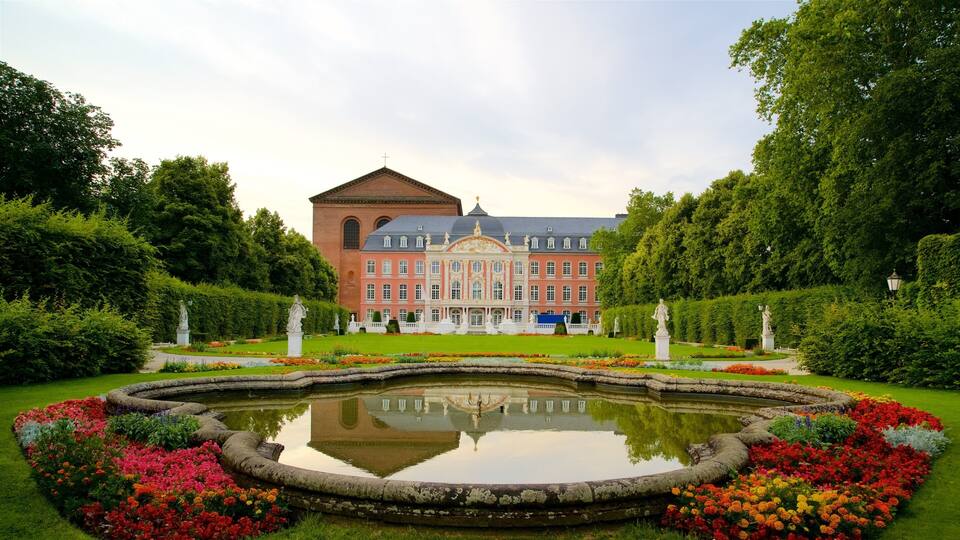 A large, ornate building with a central dome, surrounded by a formal garden with a reflecting pond and colorful flower beds.