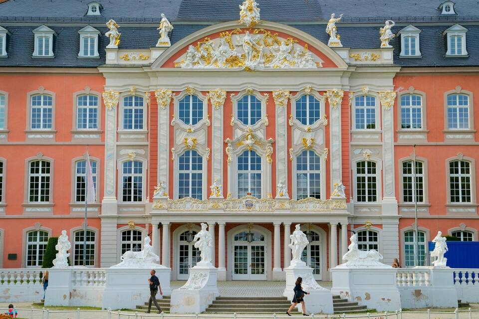 A grand building with ornate gold decorations, large windows, and statues.