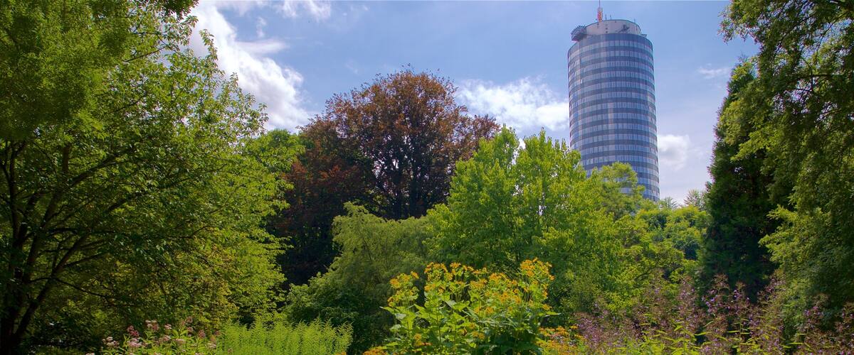 A park with lush greenery, a variety of flowering plants, and a modern building in the background.