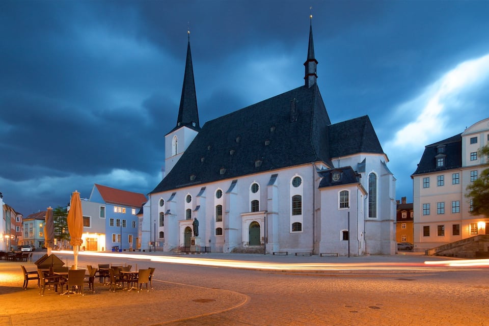 A historic church with two spires, a cobblestone street, and traditional European buildings.