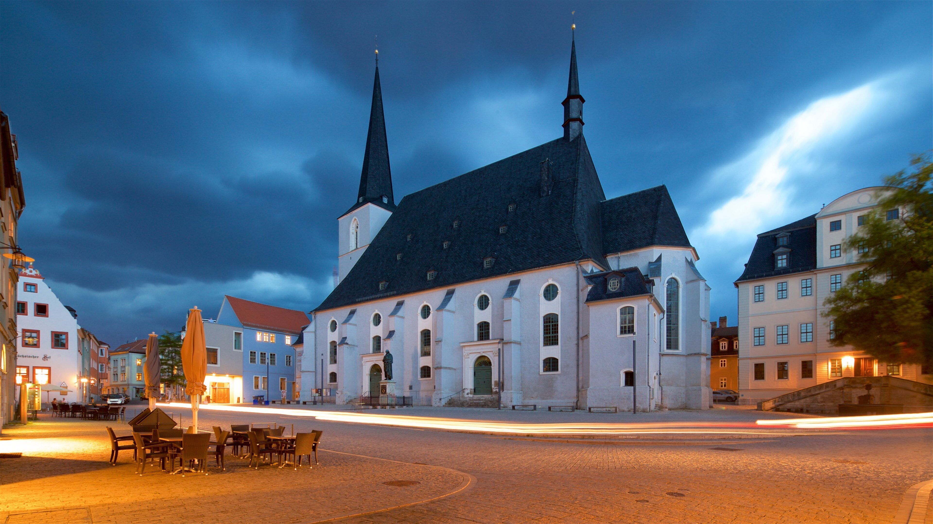 A historic church with two spires, a cobblestone street, and traditional European buildings.