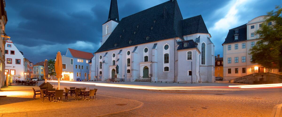 A historic church with two spires, a cobblestone street, and traditional European buildings.