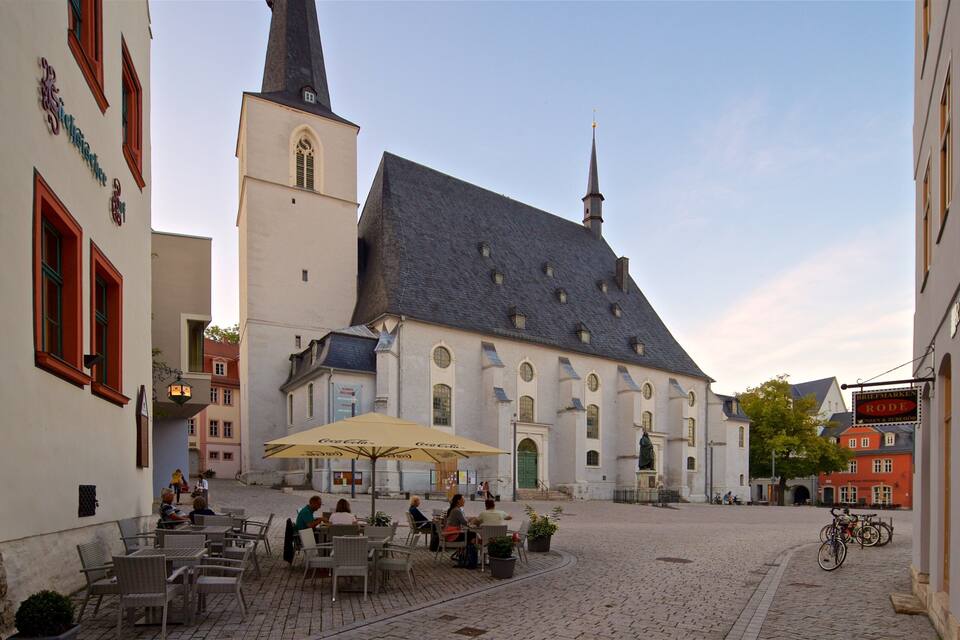 Una plaza adoquinada con una iglesia, mesas al aire libre y bicicletas.