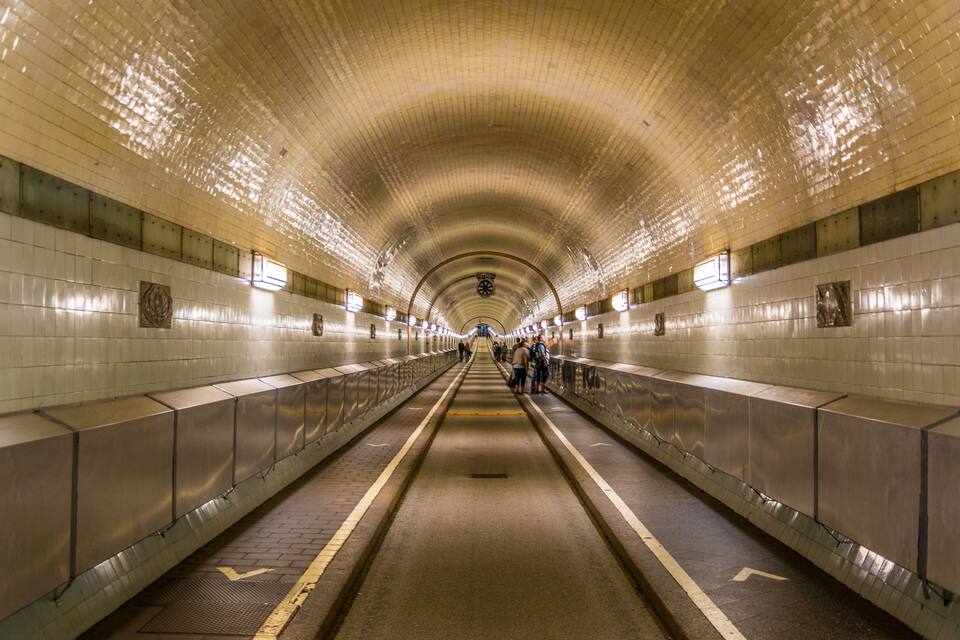 A subway station with tiled walls, a curved ceiling, and a central walkway.