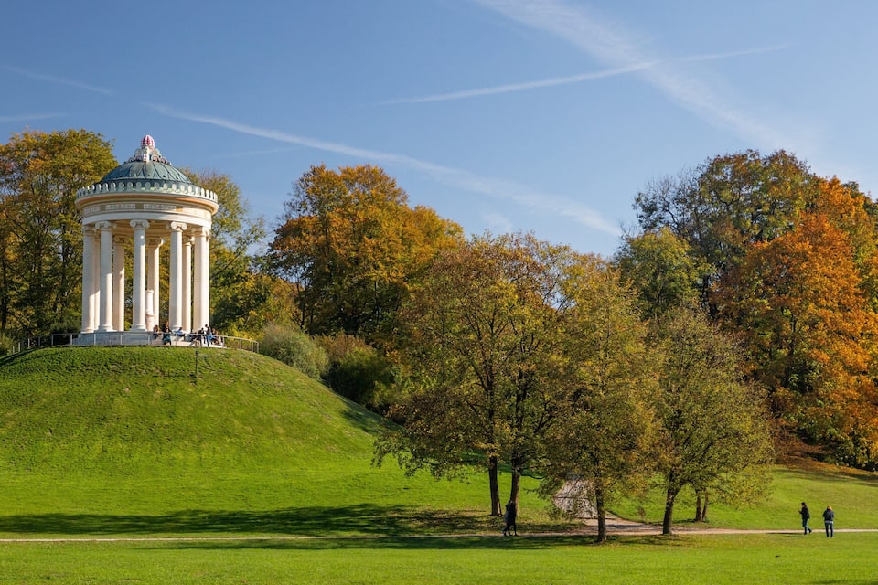 A white neoclassical pavilion on a grassy hill with autumn-colored trees in the background.