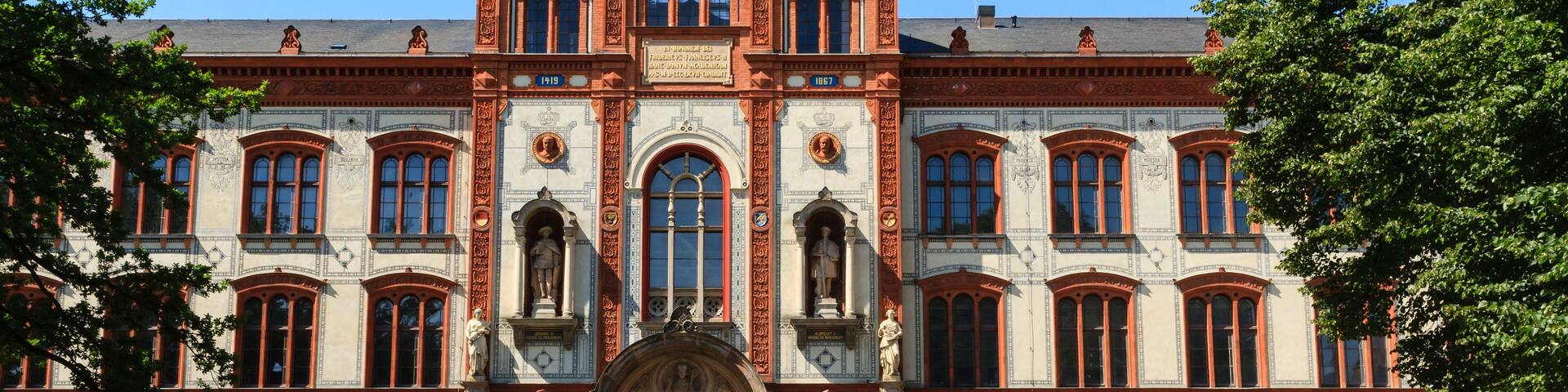 Un edificio grande y ornamentado con múltiples ventanales de arco y estatuas, rodeado de césped y árboles.