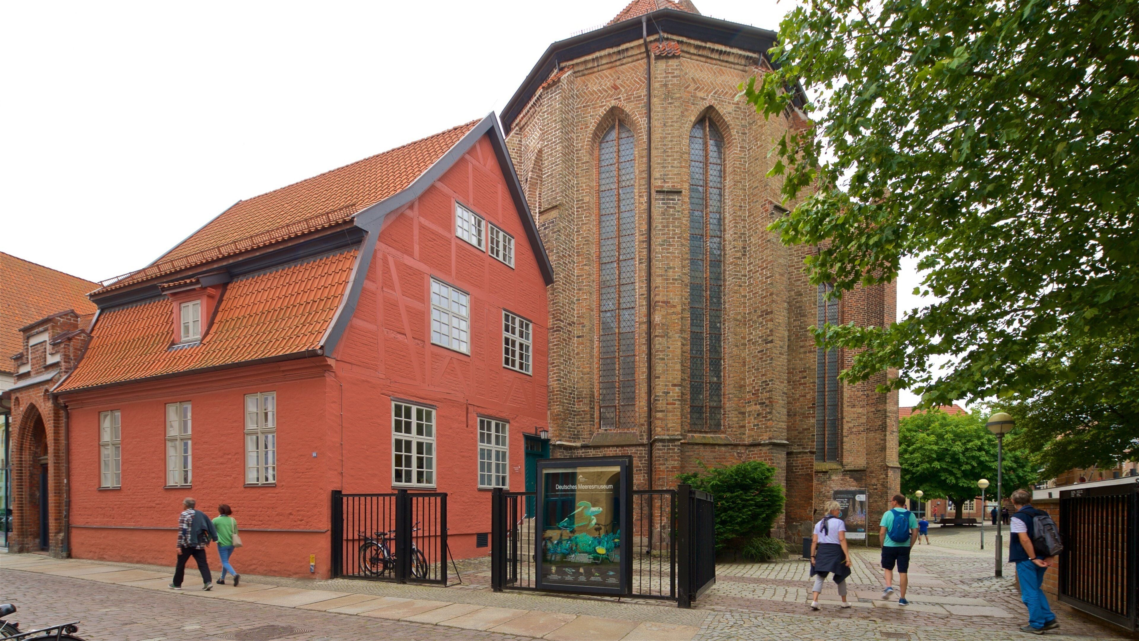 Ein Gebäude aus roten Ziegeln mit einem Ziegeldach und einem hohen, schmalen Turm mit rundbogenförmigen Fenstern.