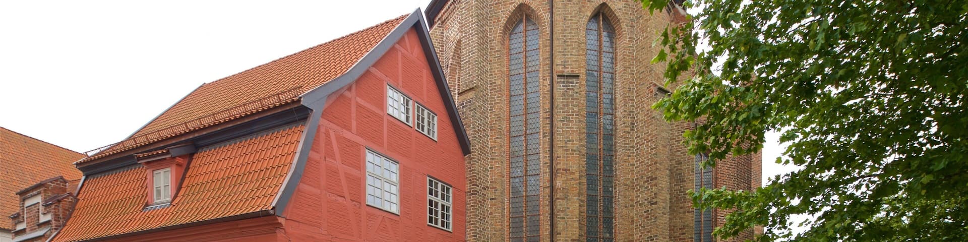 A red brick building with a tiled roof and a tall, narrow tower with arched windows.