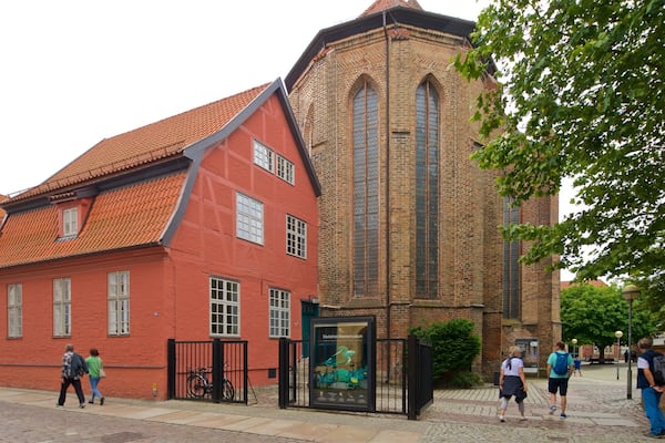 Ein Gebäude aus roten Ziegeln mit einem Ziegeldach und einem hohen, schmalen Turm mit rundbogenförmigen Fenstern.