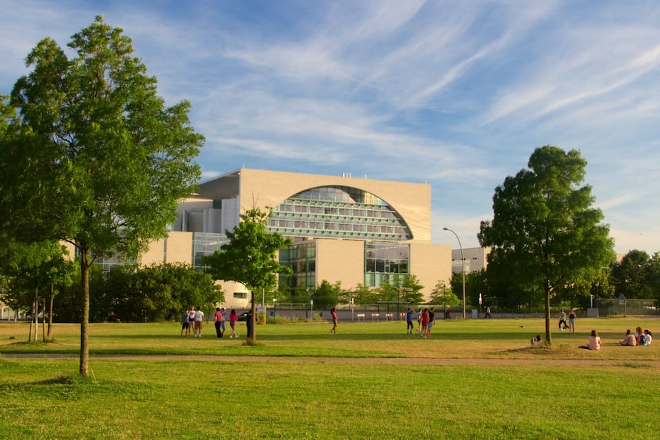 Un bâtiment moderne doté d’un grand dôme de verre, avec un parc où l’on aperçoit des personnes et des arbres au premier plan.