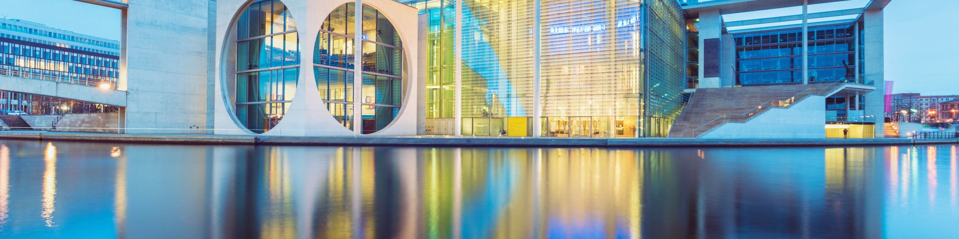 Um edifício de arquitetura moderna com janelas circulares e uma piscina refletora na frente.