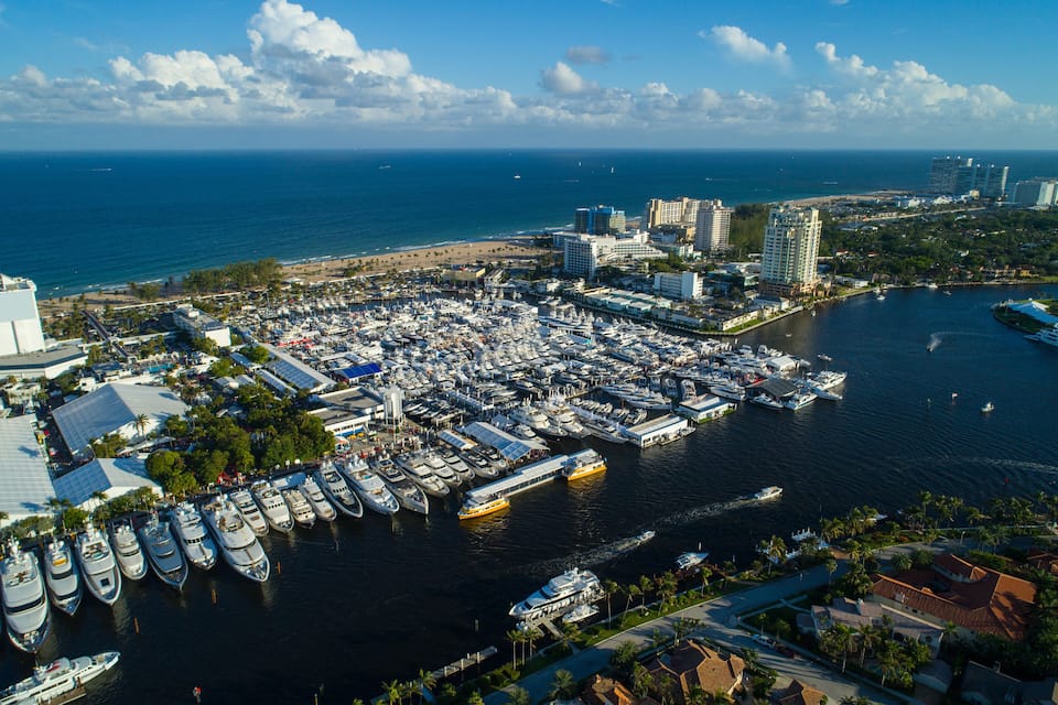 A marina with numerous boats docked, a beach, and buildings along the coastline.