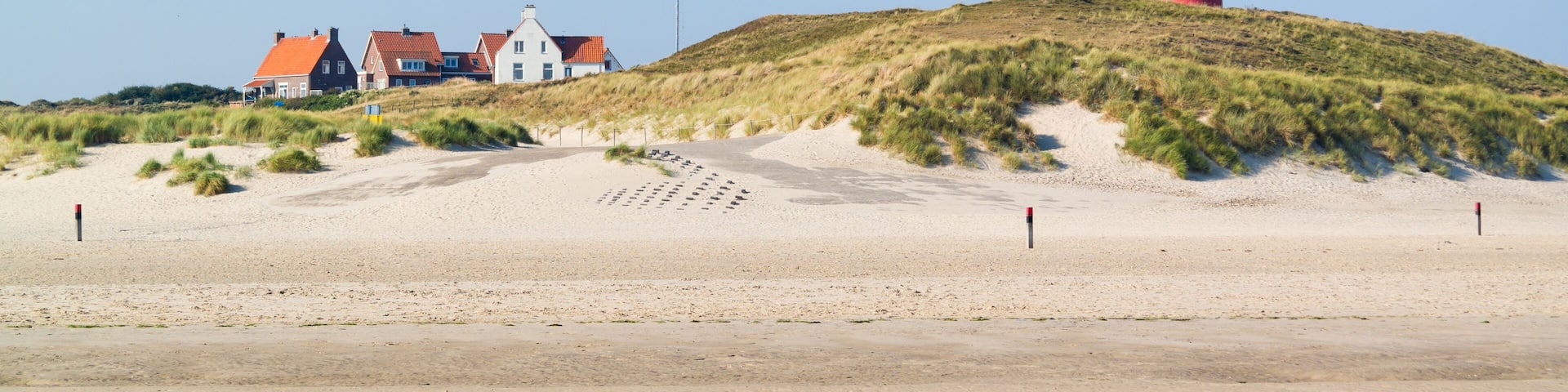 A red lighthouse on a sandy hill with houses in the background.