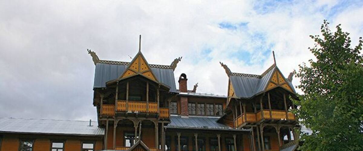 A large, ornate wooden house with multiple balconies and a steeply pitched roof.