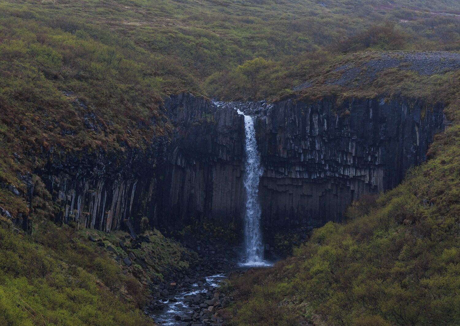 I believe this is where this waterfall is. What you are seeing is a rhyolite rock waterfall. Rhyolite forms when lava heats in a way that mimics mud. Crystals form and can be in any direction. this waterfall is called the black waterfall. 