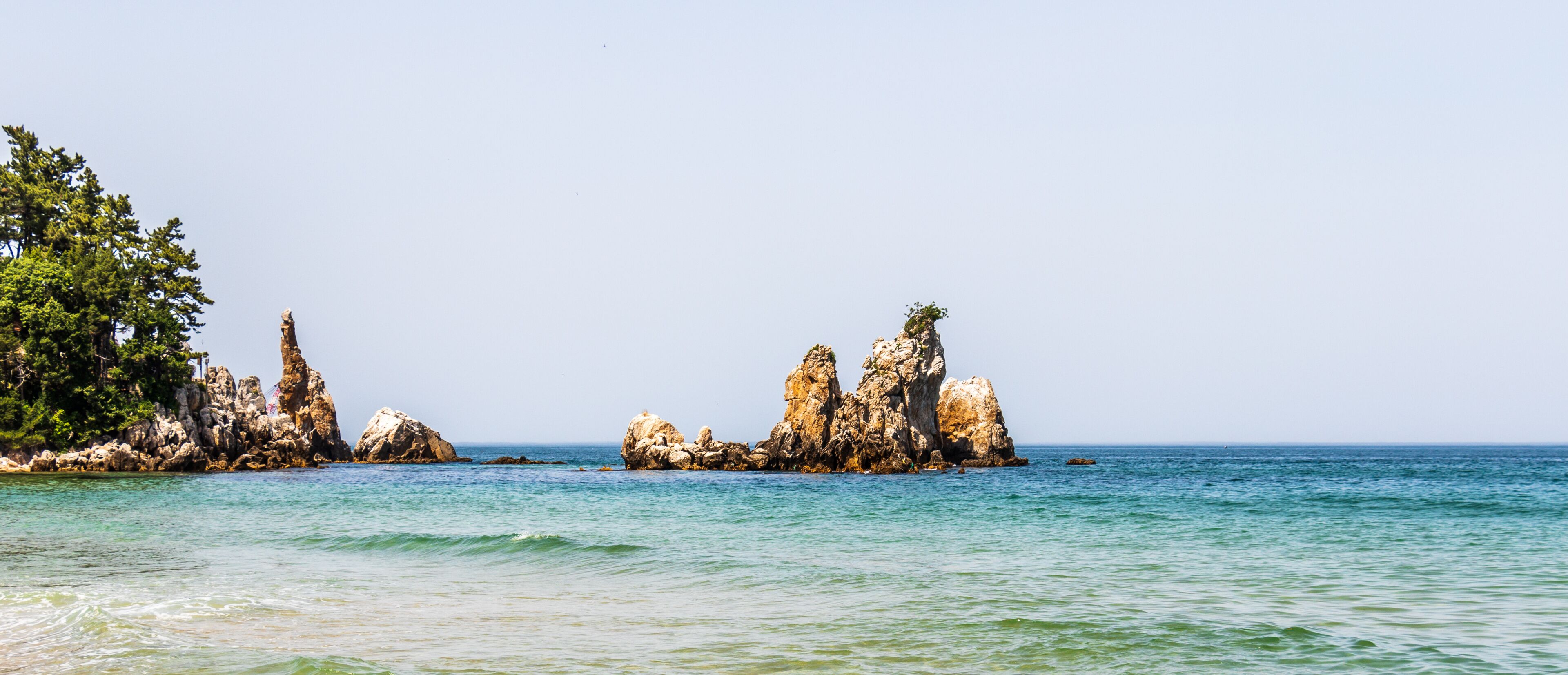 A coastal landscape with rocky formations and clear blue water.