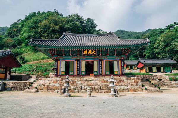 Ein traditioneller koreanischer Tempel mit aufwendiger Architektur, Steinstufen und einer Steinsäule vor der Fassade.
