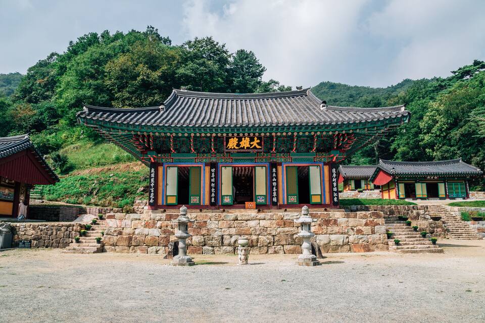 Un templo coreano tradicional con arquitectura ornamentada, escalones de piedra y un farolillo de piedra al frente.