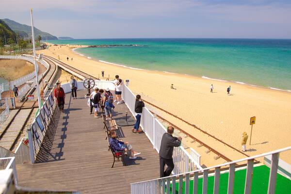 A wooden boardwalk with people walking along it, overlooking a sandy beach and turquoise waters.