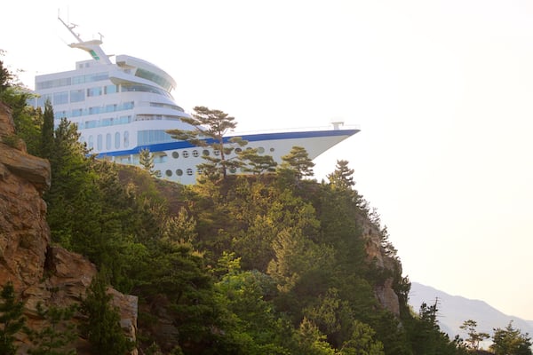 A modern building with a unique, curved design, surrounded by lush greenery and rocky terrain.