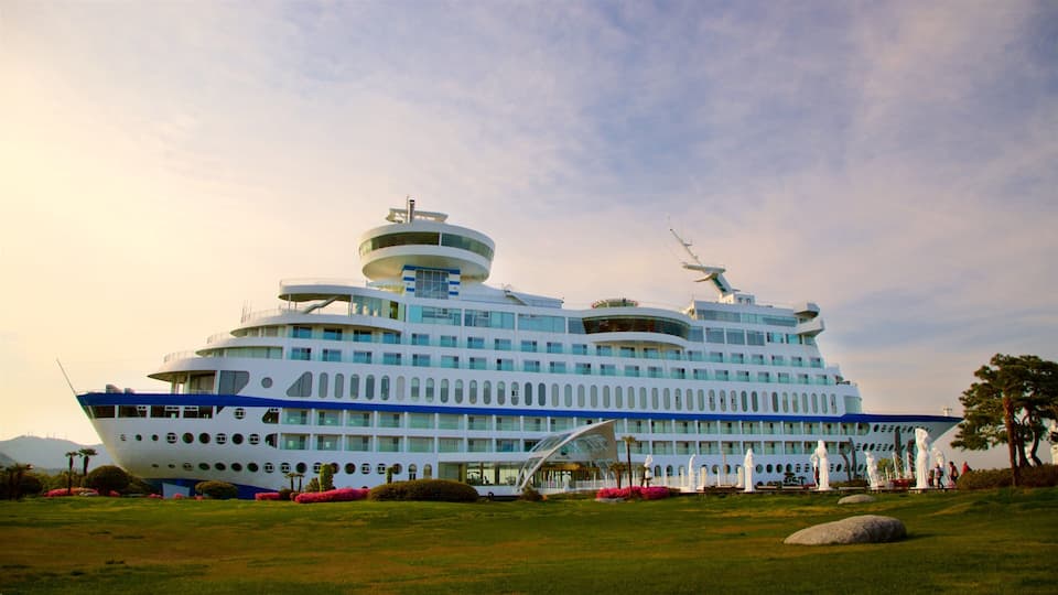 A large cruise ship docked at a port with a landscaped area featuring statues and a clear sky.