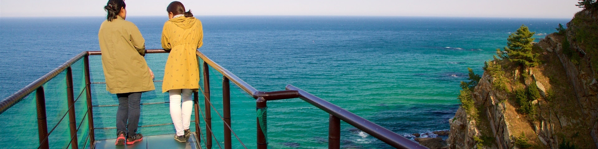 Two people on a glass bridge overlooking a turquoise sea.