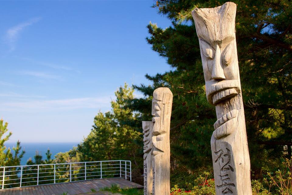 Two wooden totem poles with carvings, set against a backdrop of trees and a clear sky.