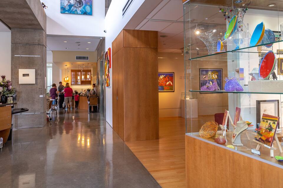 Interior de una galería de arte con pisos de madera, vitrinas de vidrio y diversas obras de arte.