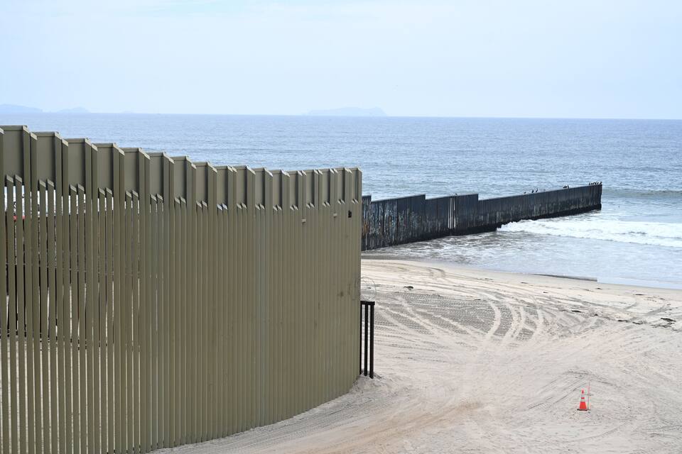 Una platja amb un mur de formigó i un moll de fusta.