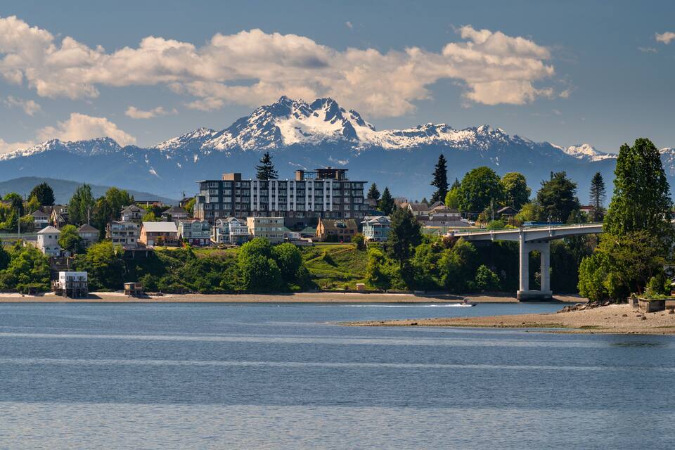 A riverside town with a bridge, a mountain range, and a large hotel.
