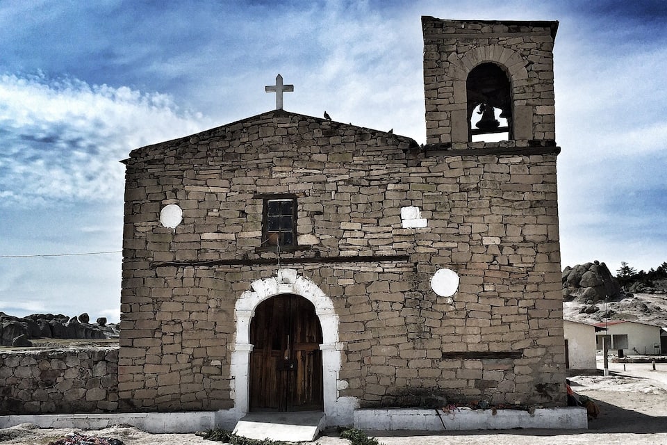 Una pequeña iglesia de piedra con un campanario y una cruz en la parte superior.