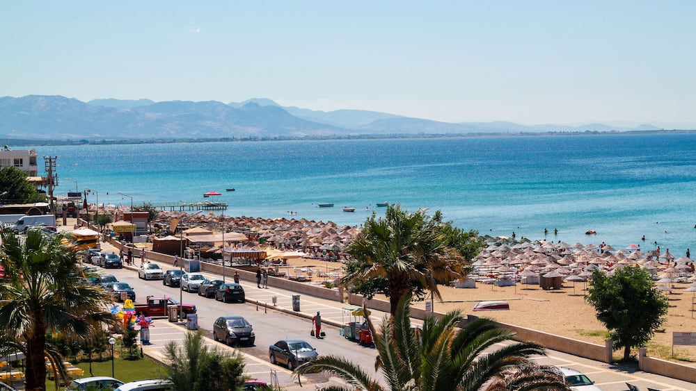 Un paysage urbain côtier avec une plage, des palmiers et des montagnes en arrière-plan.