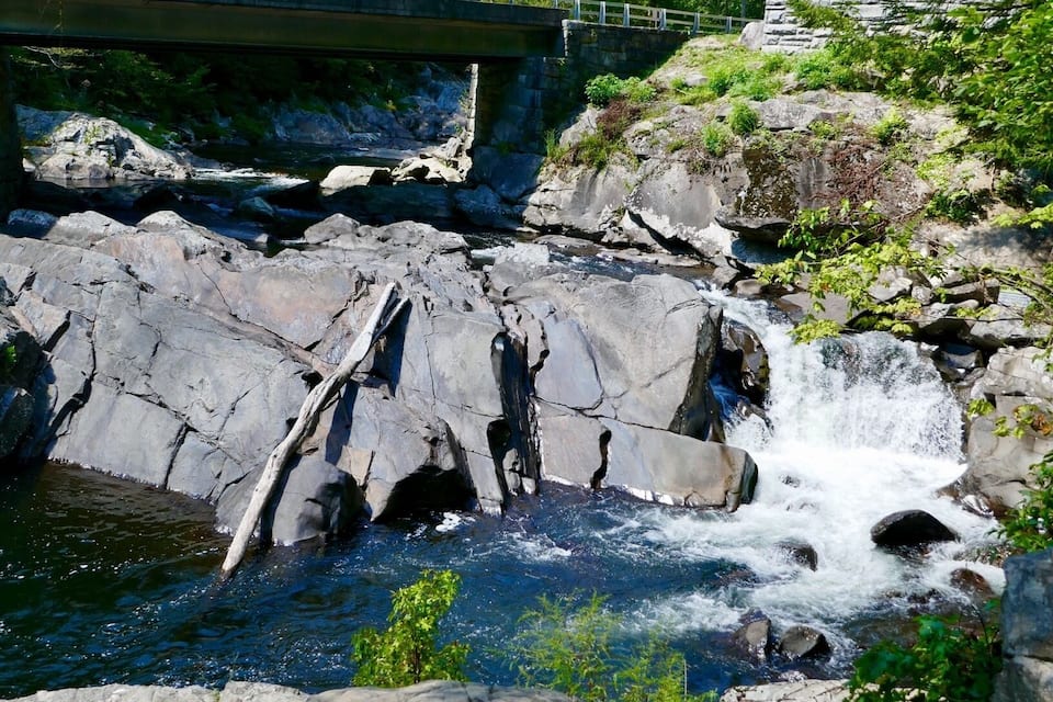Uma cascata rochosa com uma ponte ao fundo.