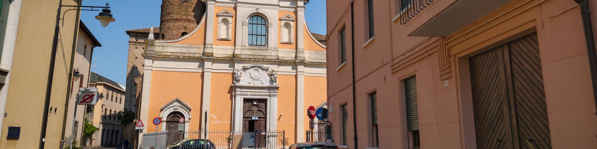 A cobblestone street with a church featuring a tall bell tower and a parked car.