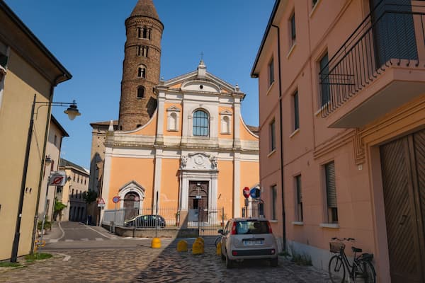 Eine Kopfsteinpflasterstraße mit einer Kirche, die einen hohen Glockenturm und einen parkenden Wagen hat.