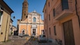 Una strada acciottolata con una chiesa caratterizzata da un alto campanile e un'auto parcheggiata.