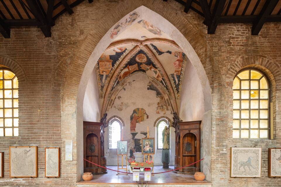 Ein Kircheninneres mit Gewölbedecke, Backsteinwänden und religiöser Kunst.