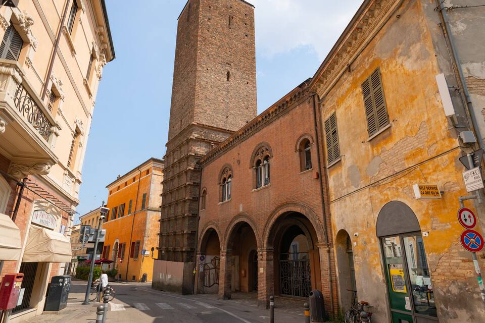 A narrow street with historic buildings, including a tall brick tower and a building with arched windows.