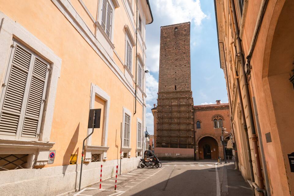 A narrow street with a tall brick tower in the background.