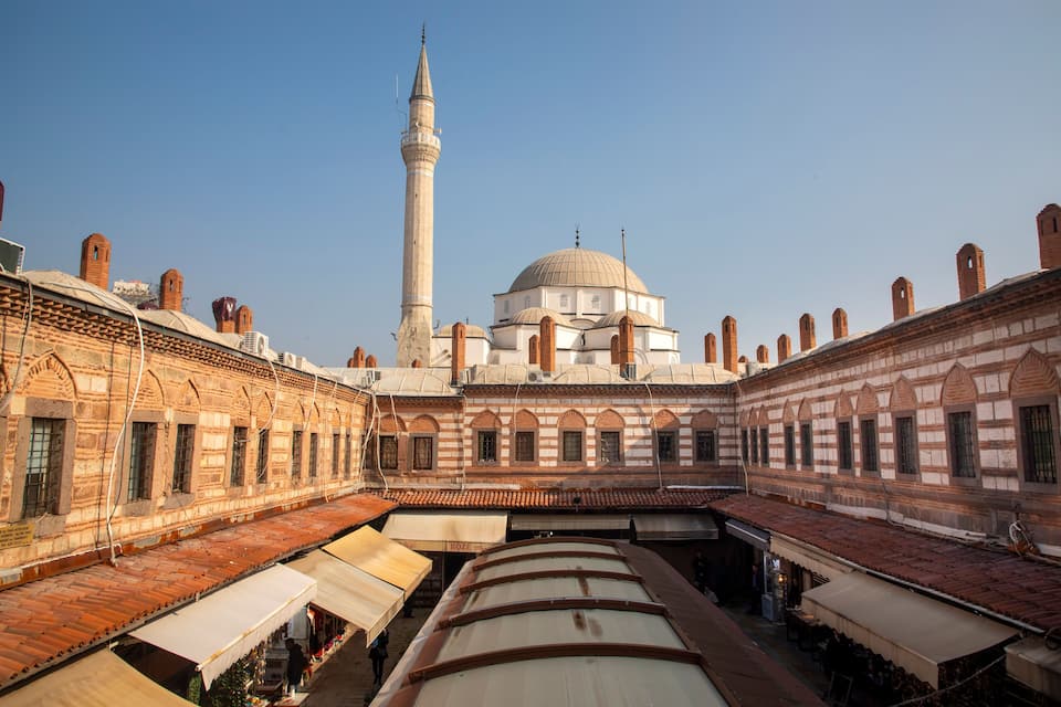 En moské med et højt minaret og en kuppel, omgivet af overdækkede markedsboder.