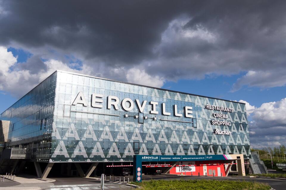 Um edifício moderno com o nome 'AEROVILLE' e indicações para restaurantes, cinema e lojas.