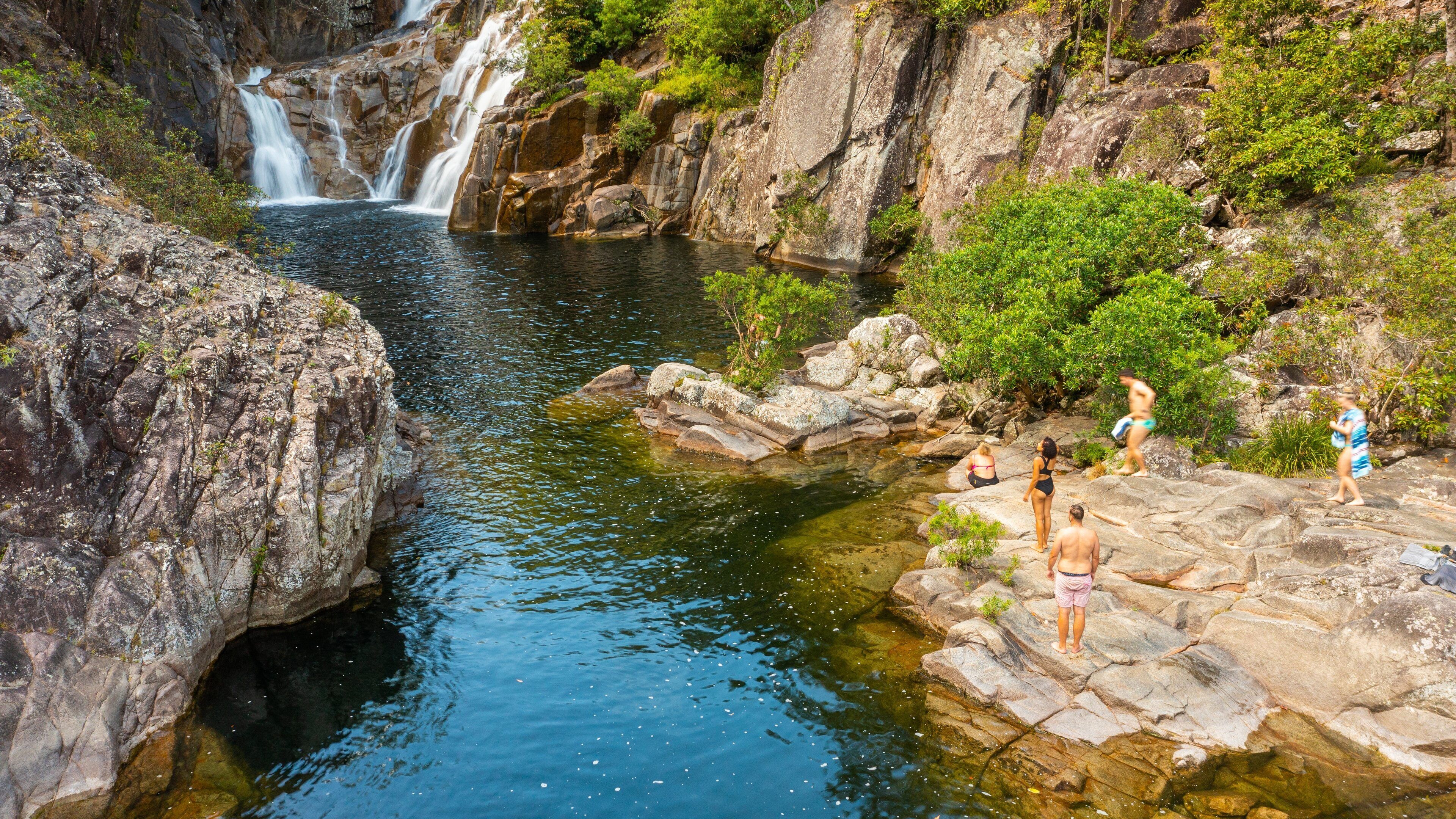 A waterfall cascading into a clear pool surrounded by rocky terrain and lush greenery.