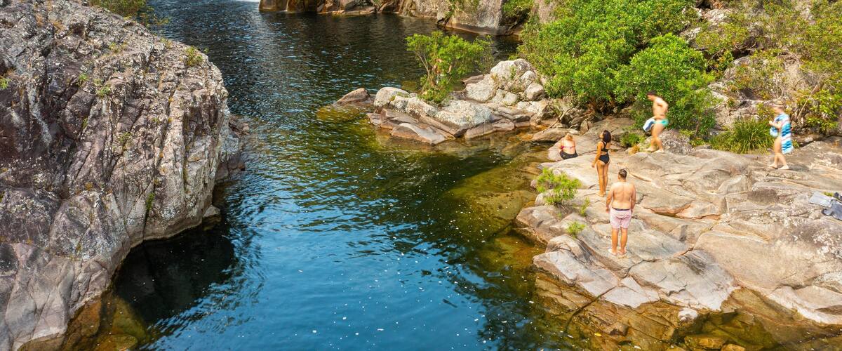 A waterfall cascading into a clear pool surrounded by rocky terrain and lush greenery.