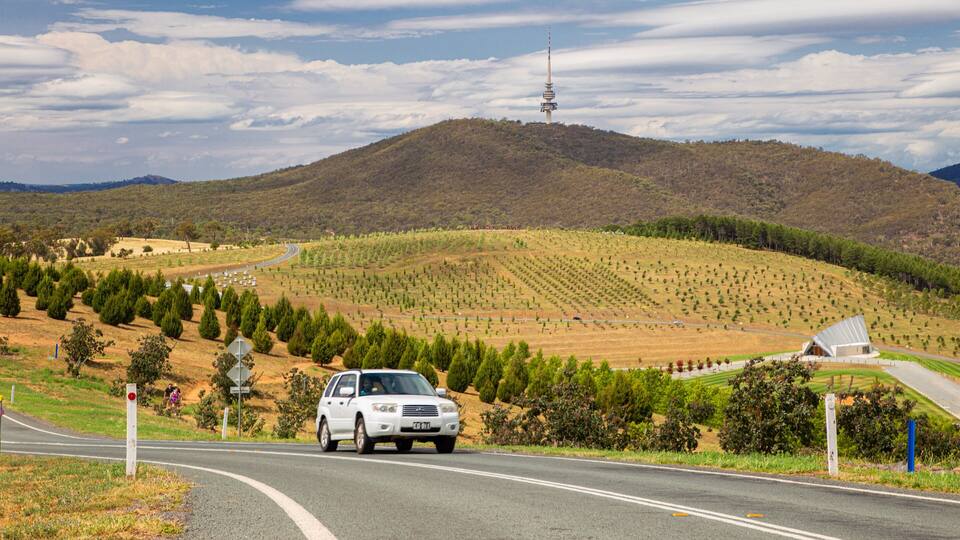 A white SUV driving on a road with a mountainous landscape in the background.