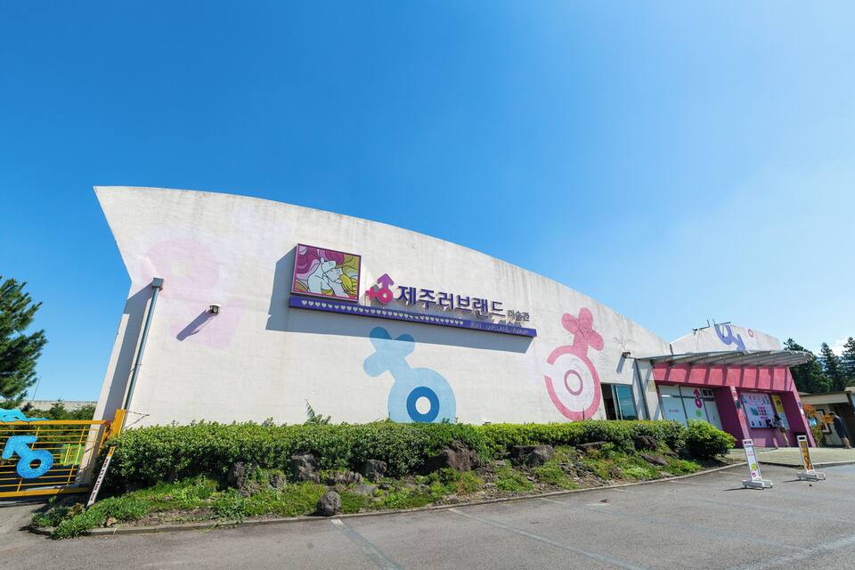 A building with a large mural, a sign with Korean text, and a parking lot.