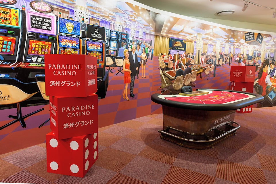 Ein Casino mit Spielautomaten, Roulette-Tischen und einer großen, roten Leuchtreklame für Paradise Casino.