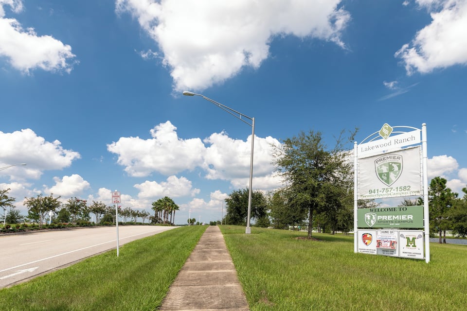 A road with a 'No Parking' sign, a 'Welcome to Premier Sports Campus' sign, and a street lamp.